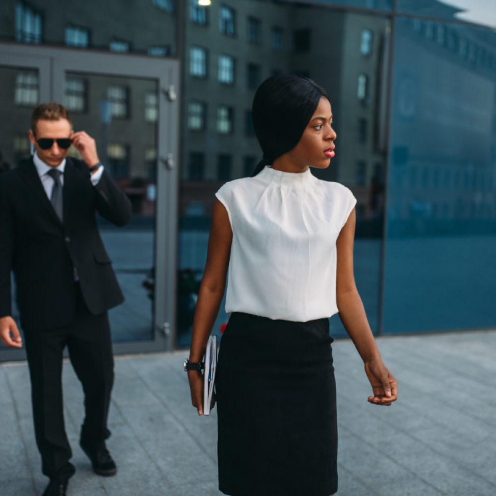 Business woman, bodyguard in suit on background Black business woman bodyguard in suit and sunglasses on background. Security guard is a risky profession, protection of VIPs, guarding occupation, private safety